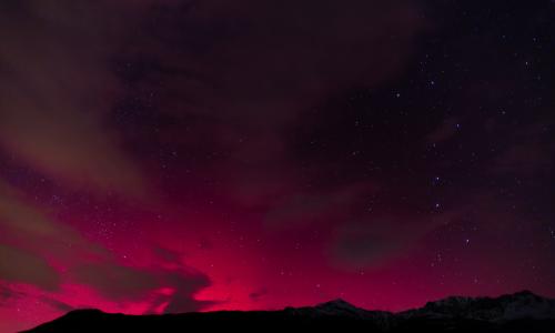 Aurore rouge vif embrasant l’horizon sous de longs nuages sombres, au-dessus d’une ligne de collines