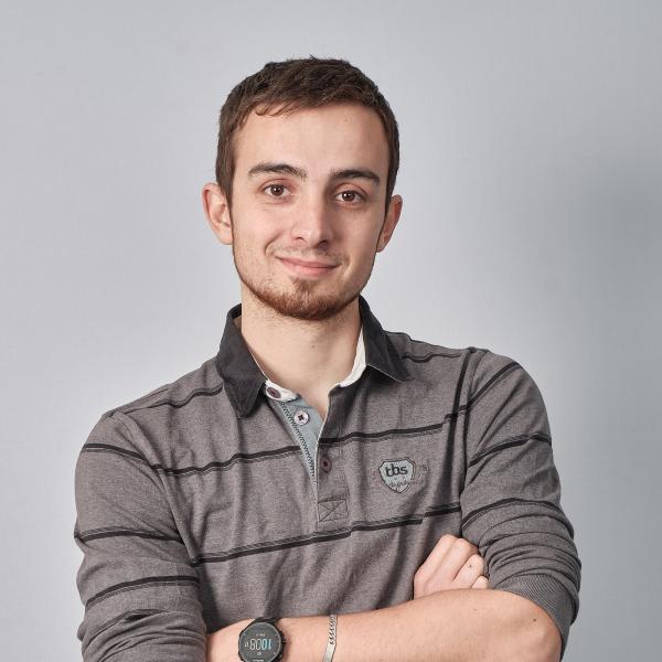 Jérôme souriant, bras croisés, en polo gris à rayures, devant un fond gris clair