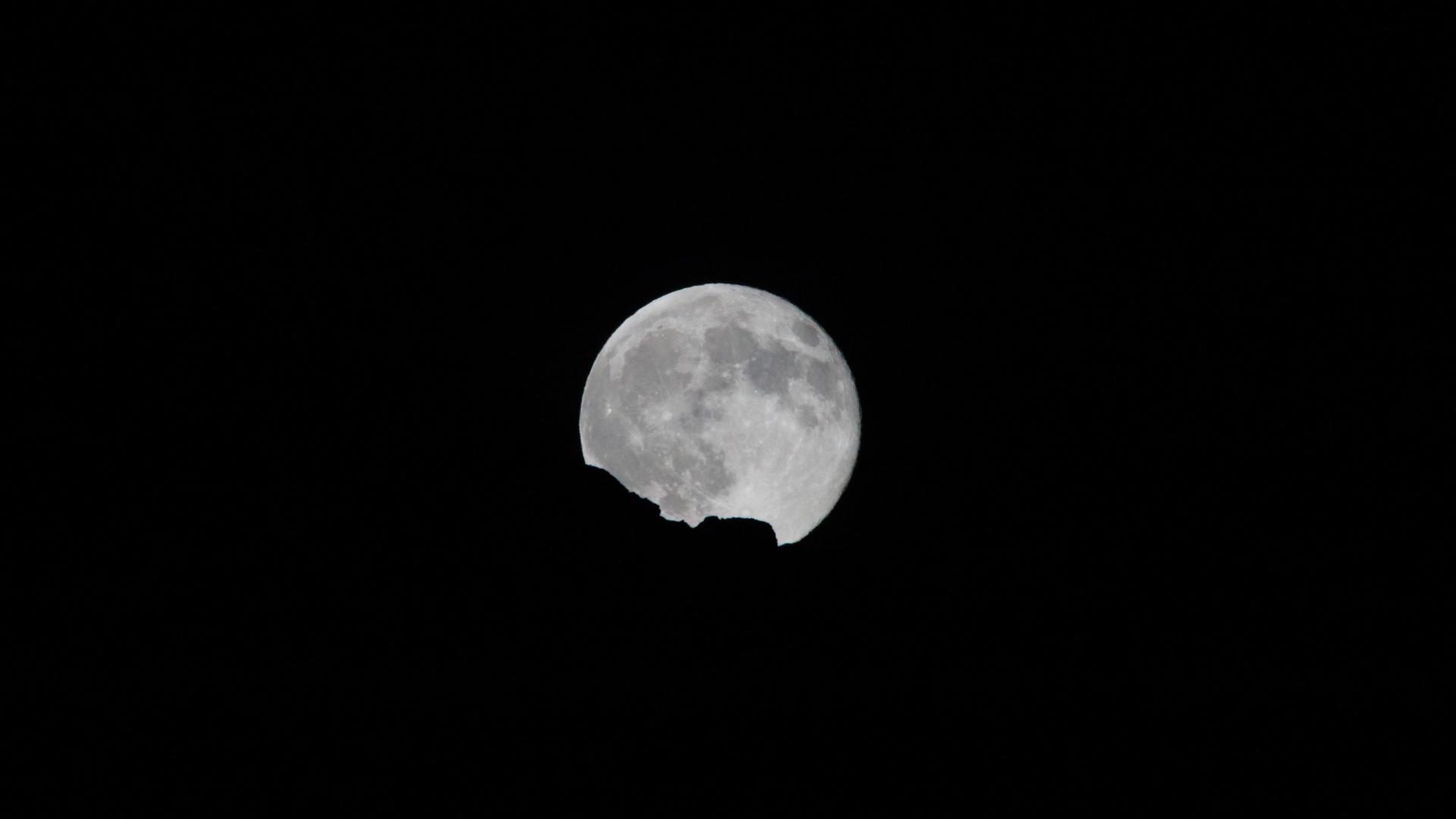 Pleine lune se levant derrière une crête, sur un ciel noir