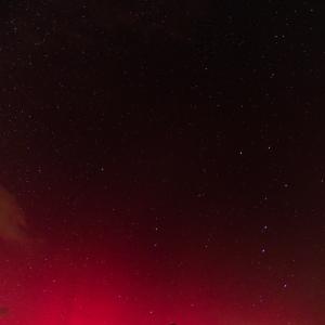 Lueur rouge intense d’une aurore boréale au-dessus d’une ligne de montagnes noires, sous un ciel étoilé