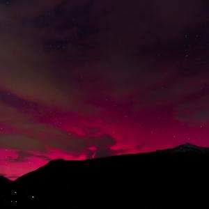 Ciel nocturne embrasé d’un rouge intense entre les nuages, au-dessus de la silhouette noire d’une colline