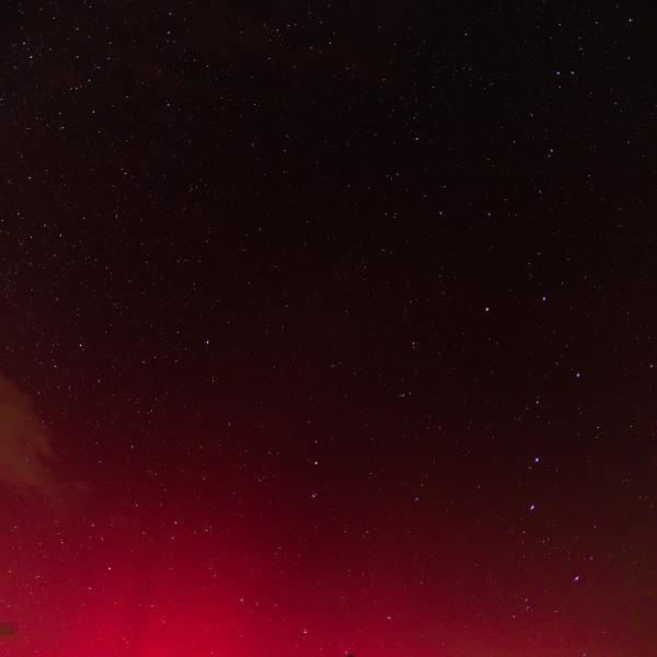 Lueur rouge intense d’une aurore boréale au-dessus d’une ligne de montagnes noires, sous un ciel étoilé