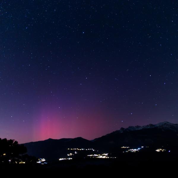Colonnes de lumière rose et violette s’élevant au-dessus d’une chaîne de montagnes, villages éclairés en contrebas