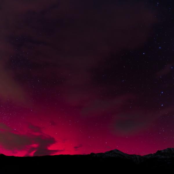 Aurore rouge vif embrasant l’horizon sous de longs nuages sombres, au-dessus d’une ligne de collines
