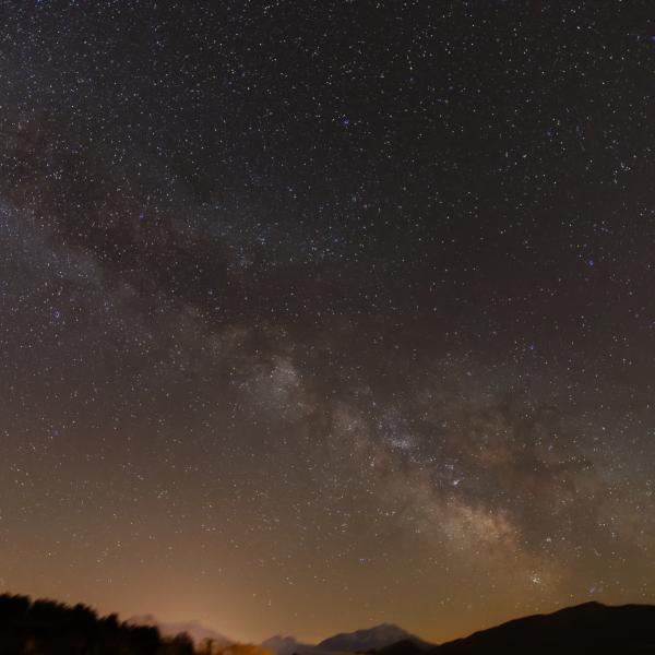 Voie lactée traversant le ciel étoilé au-dessus d’une ligne de montagnes sombres, lueur orangée à l’horizon